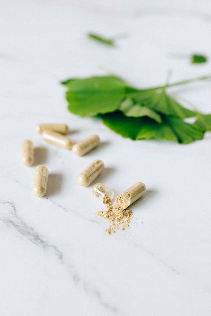 Herbal capsules and ginkgo leaf on a marble surface, representing natural supplements.